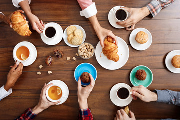Picture of people's hands on wooden table with croissants and coffee. 
