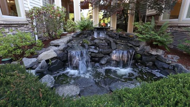 Waterfall garden feature with water flowing over real rocks into a manmade pond.
