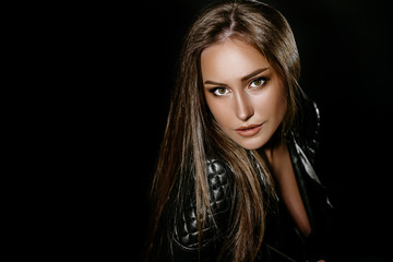 Fototapeta premium beautiful sexy brunette girl with long hair and big boobs. in the studio on a black background. Dressed in black jeans black leather jackets. girl in the image of rocker and biker. Advertising Space