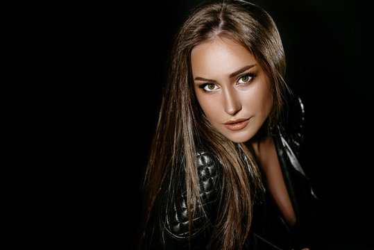 beautiful sexy brunette girl with long hair and big boobs. in the studio on a black background. Dressed in black jeans black leather jackets. girl in the image of rocker and biker. Advertising Space