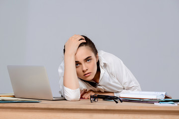 Tired young beautiful businesswoman sitting at workplace over purple background.