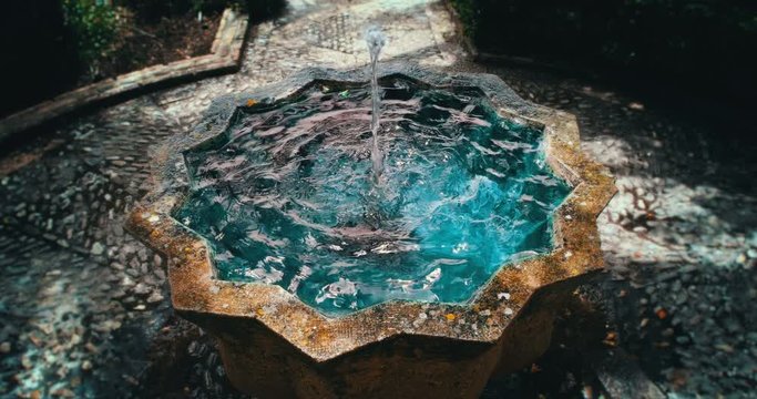 Mystical water fountain with cyan catchment on a shadowy path