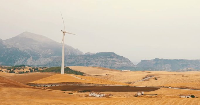 Wind turbine set in rustic dry fields on a hazy day with old farm house in FG