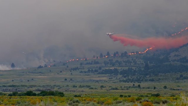 A Plane Dropping Fire Retardant On A Forest Fire Burning A Mountainside In California.