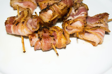 Rolls of slices of cooked bacon subject with a toothpick