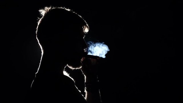 Video as a man smokes a big cigar. Black. Silhouette. Close up. Slow motion