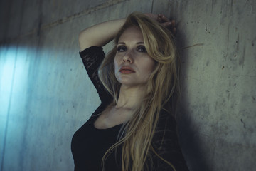 Fototapeta premium Posing, blonde dressed in skintight black costume on a gray ceme