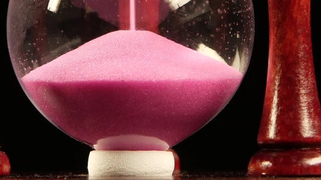 Sand is at the bottom of the clock. Black. Slow motion. Close up