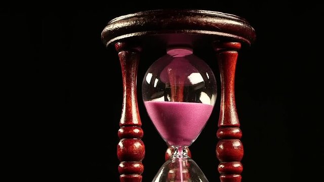 Sand falls through a bottleneck in hourglass. Black. Slow motion. Close up