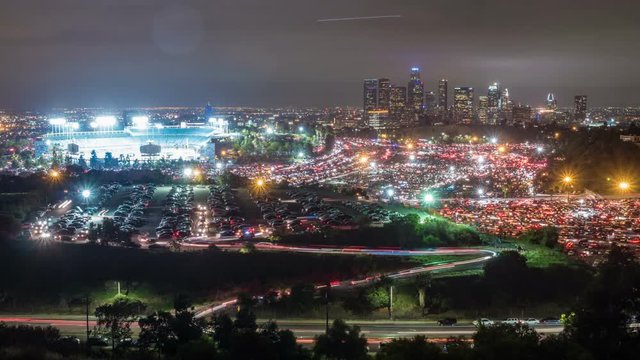 Time Lapse of huge parking lots emptying in Los Angeles. The downtown buildings are in the background. The baseball stadium and it's parking lots can be seen in the foreground as all of the cars leave.