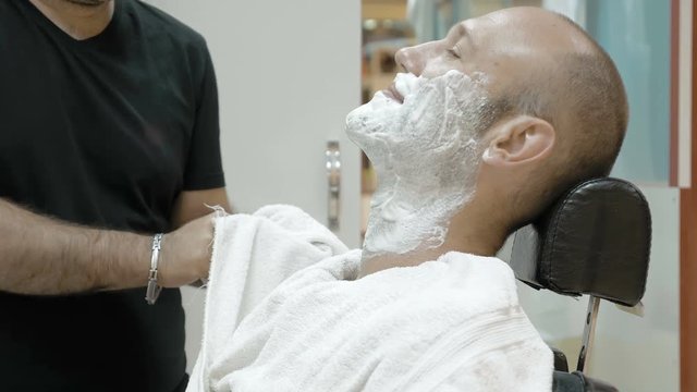 Baber or men's hair stylist in a barber shop or hair salon applied to the face shaving foam before grooming the beard and wipes his hands.