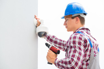 Young Male Technician Installing Camera On Wall