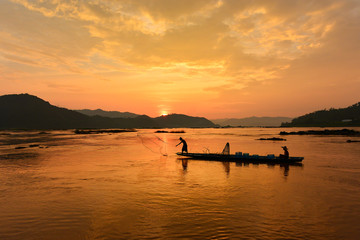 Fototapeta premium The suluate fisherman casting a net into the water during on sunset,Nongkhai Thailand