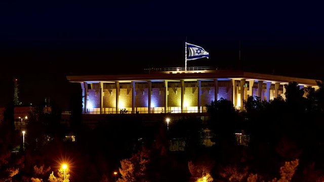 Knesset building the Parliament of Israel with flying waving flag of Israel at night. The knesset located in Jerusalem and elects both President and Prime Minister and supervises Israeli government