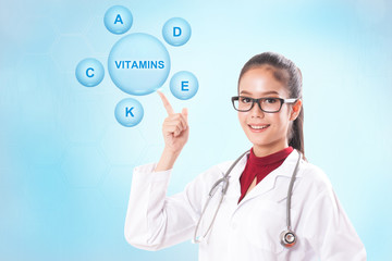 Female doctor pointing at vitamin icons on blue background. healthy concept