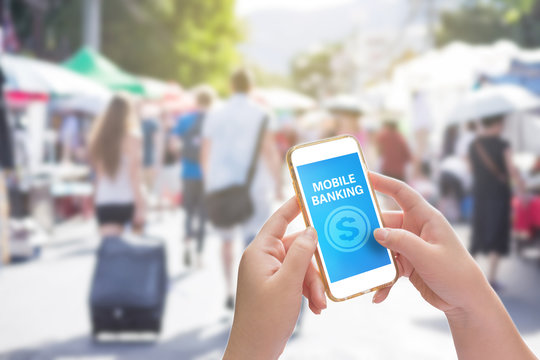 Hand holding mobile phone with Mobile banking on screen on Blurred image of street market