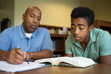 Portrait of teacher assisting a teenage student with homework in the library.