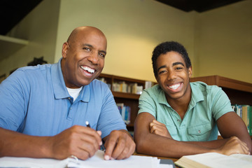 Portrait of teacher assisting a teenage student with homework in the library.