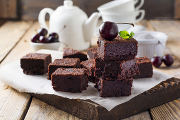 Chocolate brownies with powdered sugar and cherries on a dark wooden background. Selective focus.
