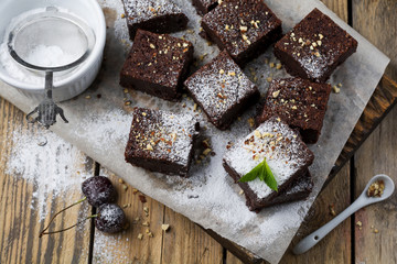 Chocolate brownies with powdered sugar and cherries on a dark wooden background. Selective focus.
