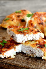 Chopped Turkey steak fried in egg batter and garnished with fresh herbs. Appetizing fried meat slices on a cutting board and an old wooden background. Closeup