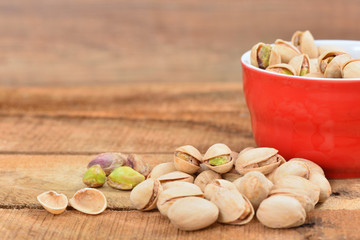 Roasted and salted pistachios in a red bowl and on a rustic table