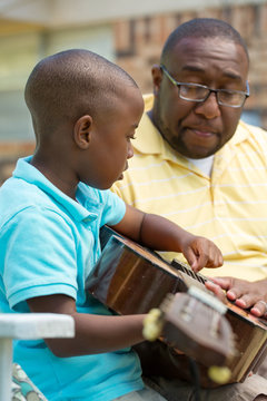 African American man teaching his son how to play the guitar
