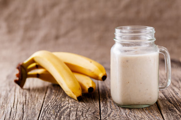 Healthy banana smoothie in glass jar with bananas on wooden tabl