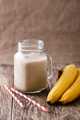 Healthy banana smoothie in glass jar with bananas on wooden tabl