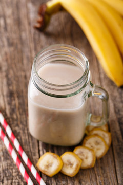 Healthy banana smoothie in glass jar with bananas on wooden tabl