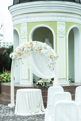 White wedding altar stands on the backyard behind an old chapel