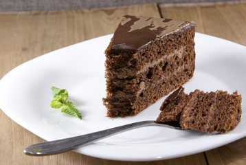 A piece of chocolate cake lying on a white plate on a rustic wooden table