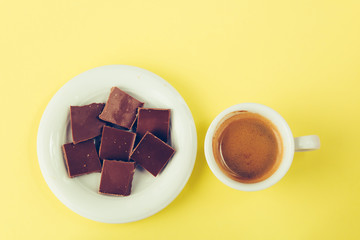 Chocolate on a saucer and a cup of coffee on a yellow surface