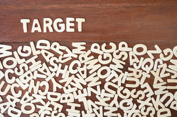 Word target made with block wooden letters next to a pile of other letters over the wooden board surface composition