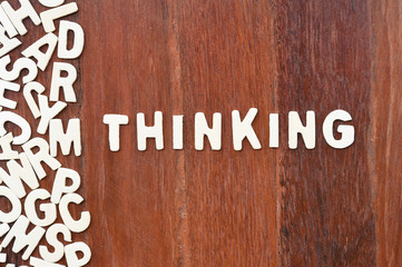 Word thinking made with block wooden letters next to a pile of other letters over the wooden board surface composition