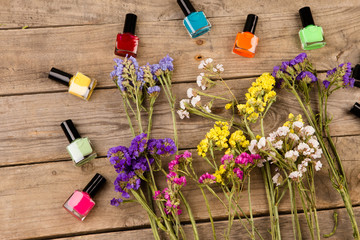 Bottles of colorful nail polish and flowers on brown wooden table