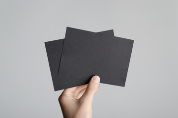 Black A6 Flyer / Postcard / Invitation Mock-Up - Male hands holding black flyers on a gray background.