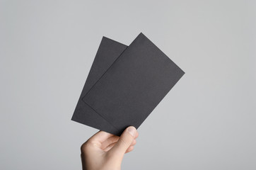 Black A6 Flyer / Postcard / Invitation Mock-Up - Male hands holding black flyers on a gray background.