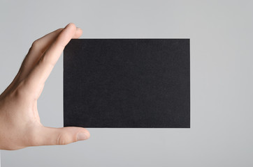 Black A6 Flyer / Postcard / Invitation Mock-Up - Male hands holding a black flyer on a gray...