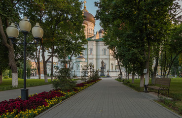 Parkway in Pervomayskiy square, Voronezh, Russia. Alley with flowers, benches and orthodox cathedral at the background.