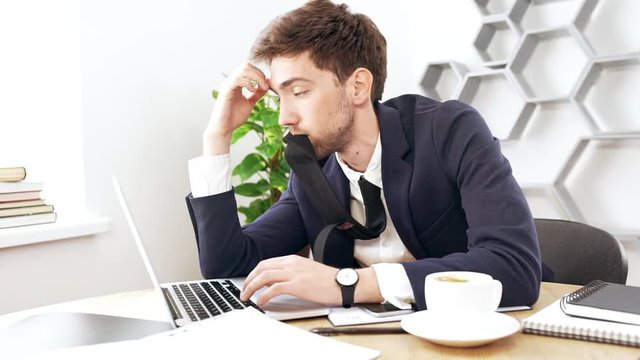 Young successful businessman working at laptop, falling asleep in office. Slow motion.