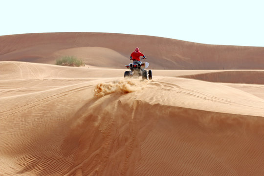 Sand flies out from under the wheels of the ATV