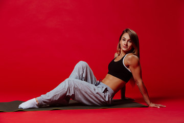 Fototapeta na wymiar Sexy fit woman in a cap posing on red background. Image of fitness woman in sports clothing. Young female model with muscular body.