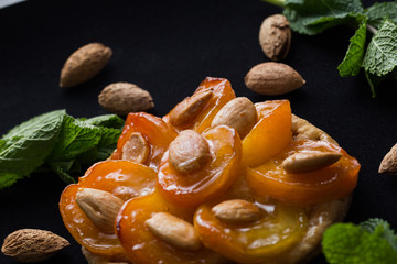 Tart with apricot and apple. Traditional french pie with fruits on dark marble background. Decorated almonds and mint leafs. Delicious dessert with copy space closeup.
