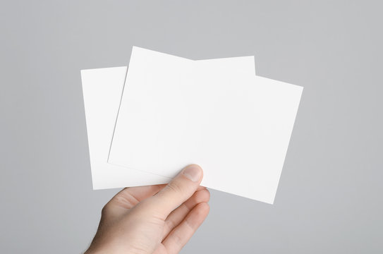 A6 Flyer / Postcard / Invitation Mock-Up - Male hands holding blank flyers on a gray background.