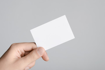 Business Card Mock-Up (85x55mm) - Male hands holding a blank card on a gray background.