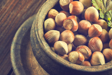 Hazelnuts in rustic round clay bowl on wooden background
