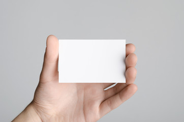 Business Card Mock-Up (85x55mm) - Male hands holding a blank card on a gray background.