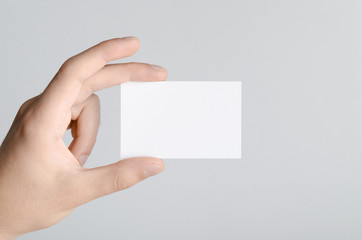 Business Card Mock-Up (85x55mm) - Male hands holding a blank card on a gray background.