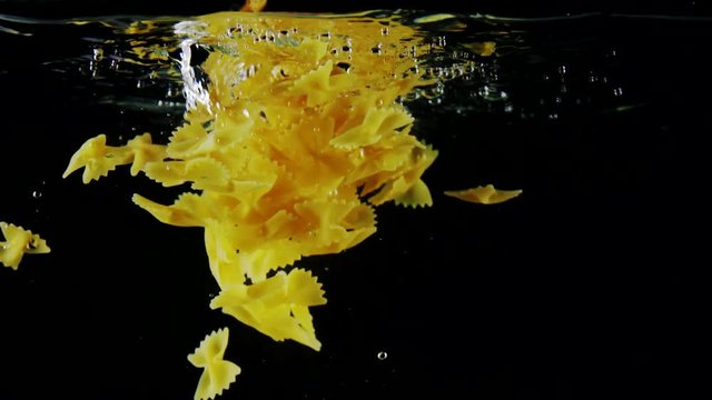 Traditional Italian cuisine slow motion farfalle pasta falling into water flying down like a butterflies on black background